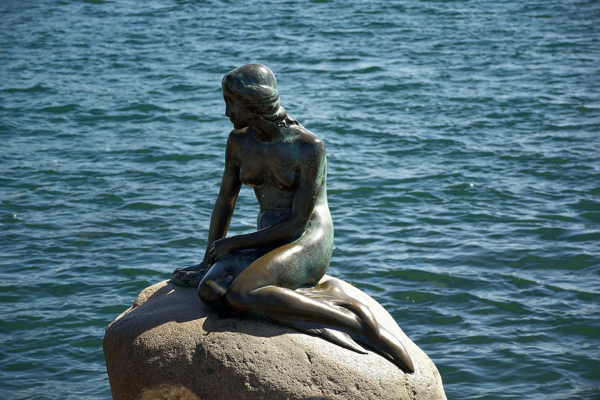 Little Mermaid statue on waterfront rocks with Copenhagen harbor background